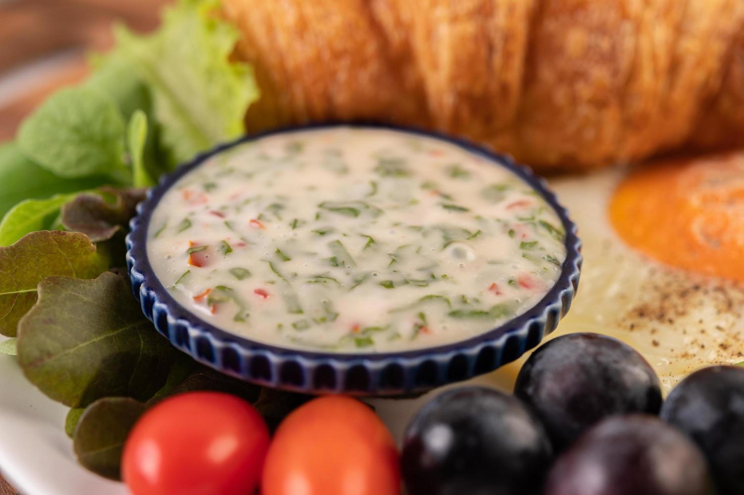 croissant, uovo fritto, condimento per insalata, uva nera e pomodori foto