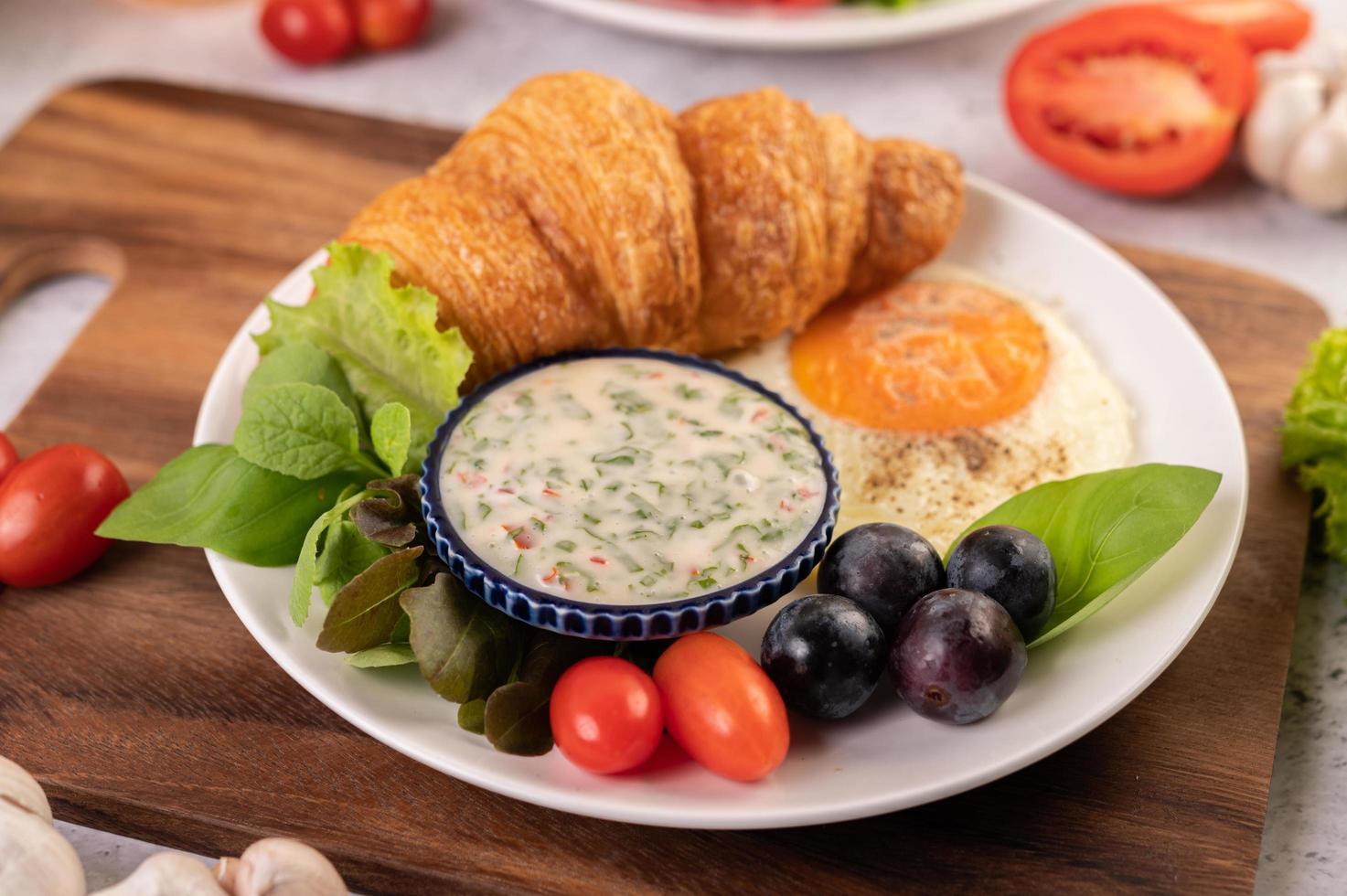 croissant, uovo fritto, condimento per insalata, uva nera e pomodori foto