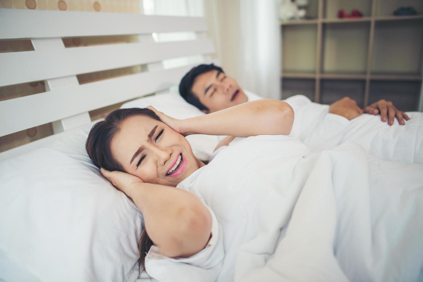 donna che dorme bloccando le orecchie con l'uomo che russa a letto foto