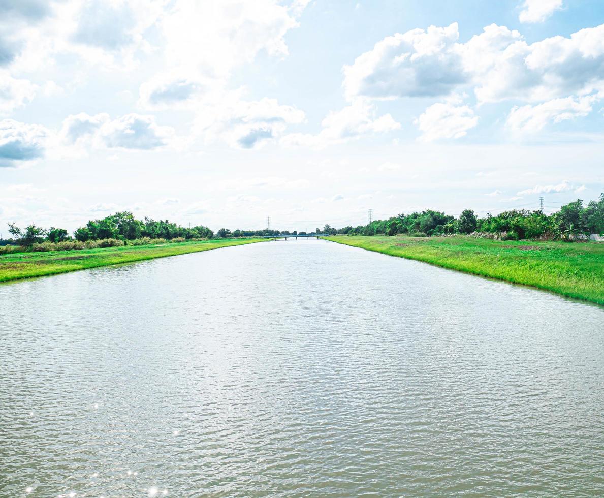 Il convogliamento dell'acqua e i canali di distribuzione .un canale di irrigazione con un sentiero che lo costeggia tra campi verdi e cielo blu. bellissimo paesaggio a banglan nakornpatum thailandia foto