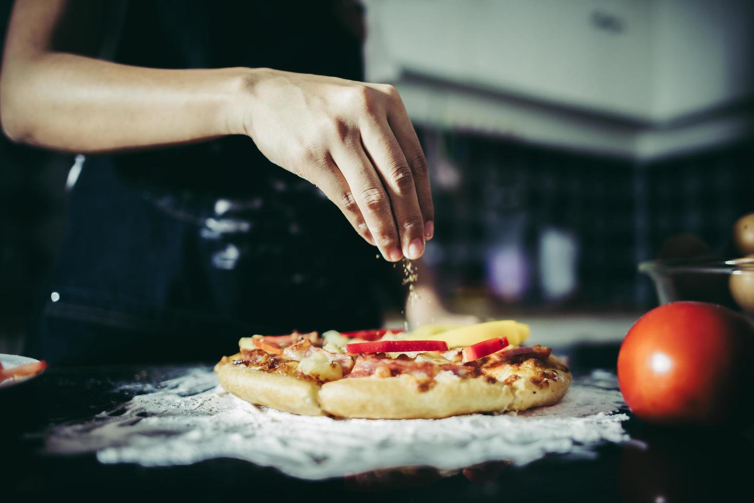 primo piano di una mano che mette l'origano sopra una pizza foto