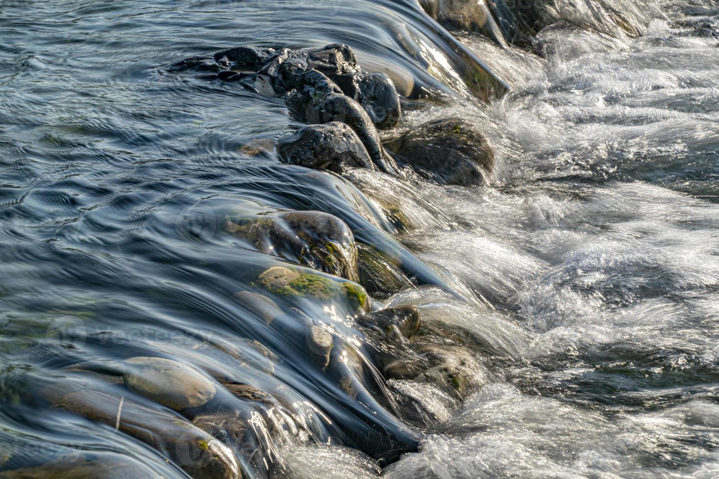 fiume flusso a tramonto dettaglio di acqua su il rocce vicino su foto