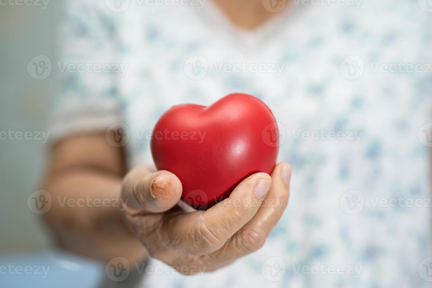 paziente asiatico anziana o anziana donna anziana che tiene il cuore rosso in mano sul letto nel reparto ospedaliero di cura, concetto medico sano e forte foto