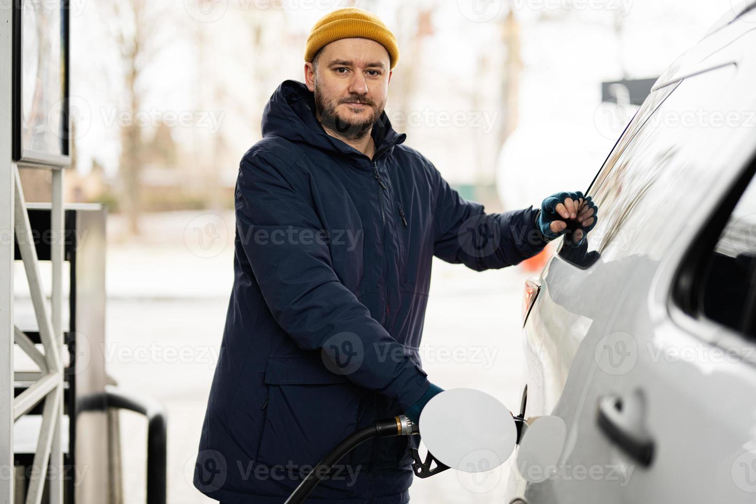 uomo rifornimento carburante il suo americano suv auto a il gas stazione nel freddo tempo atmosferico. foto