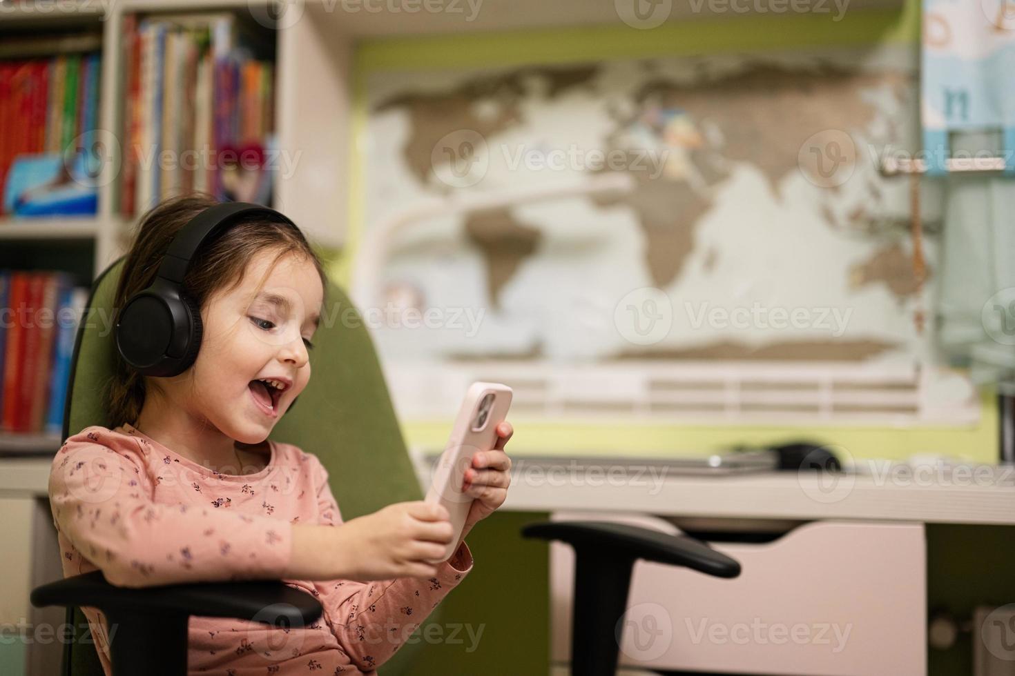 poco ragazza indossare cuffie Guardando cartoni animati o ragazzo video su sua Telefono. foto