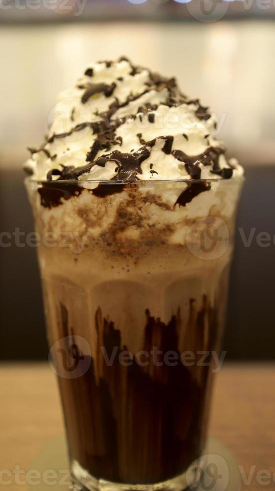 cioccolato latte shake pieno di crema e fuso cioccolato nel un' alto bicchiere a il tavolo. foto