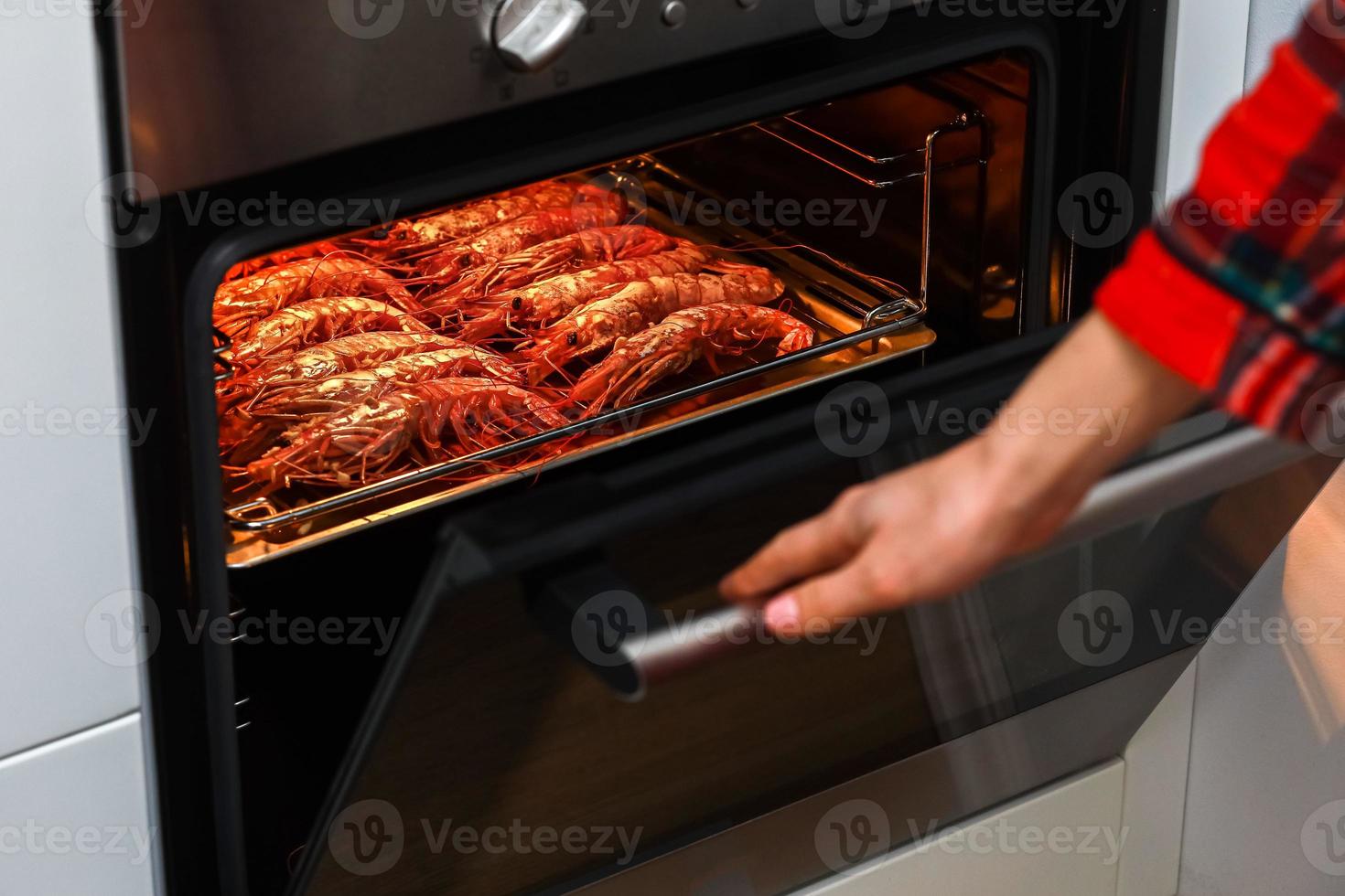 grigliato gamberetto e fritte gamberetto a casa cucina. donna Tenere un' gamberetto barbecue su un' inossidabile vassoio e cucinando nel un elettrico forno per celebrare un' notte festa. frutti di mare foto