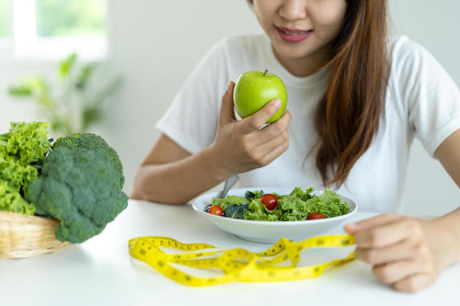 il sorridente donna gode mangiare un' insalata e Mela. per perdere peso e dieta, mangiare Alimenti quello siamo benefico per il corpo. peso perdita concetto. foto