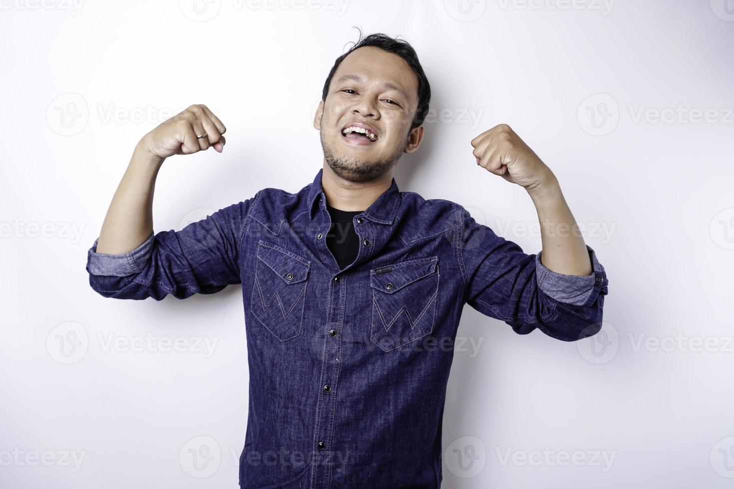 eccitato asiatico uomo indossare un' blu camicia mostrando forte gesto di sollevamento il suo braccia e muscoli sorridente con orgoglio foto