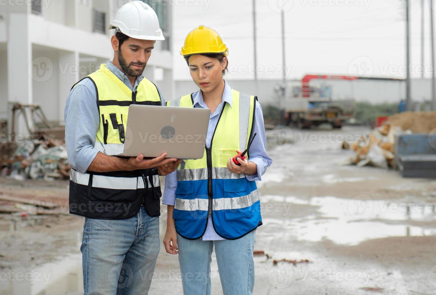 ingegnere uomo e femmina architetto indossare sicurezza caschi discutere alloggiamento sviluppo progetto a costruzione luogo utilizzando il computer portatile computer. contraente manager l'esame edificio tenuta infrastruttura. foto