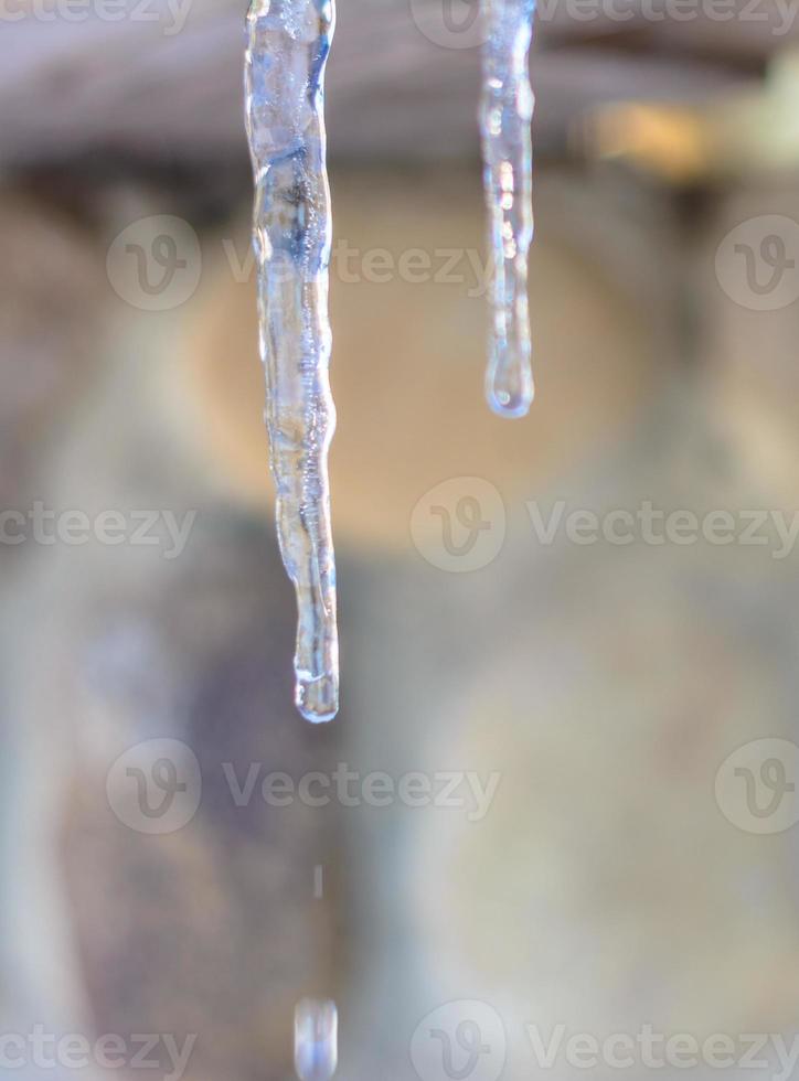 avvicinamento di un ghiacciolo mentre riscaldamento e fusione ghiaccio su il tetto di un' Casa foto