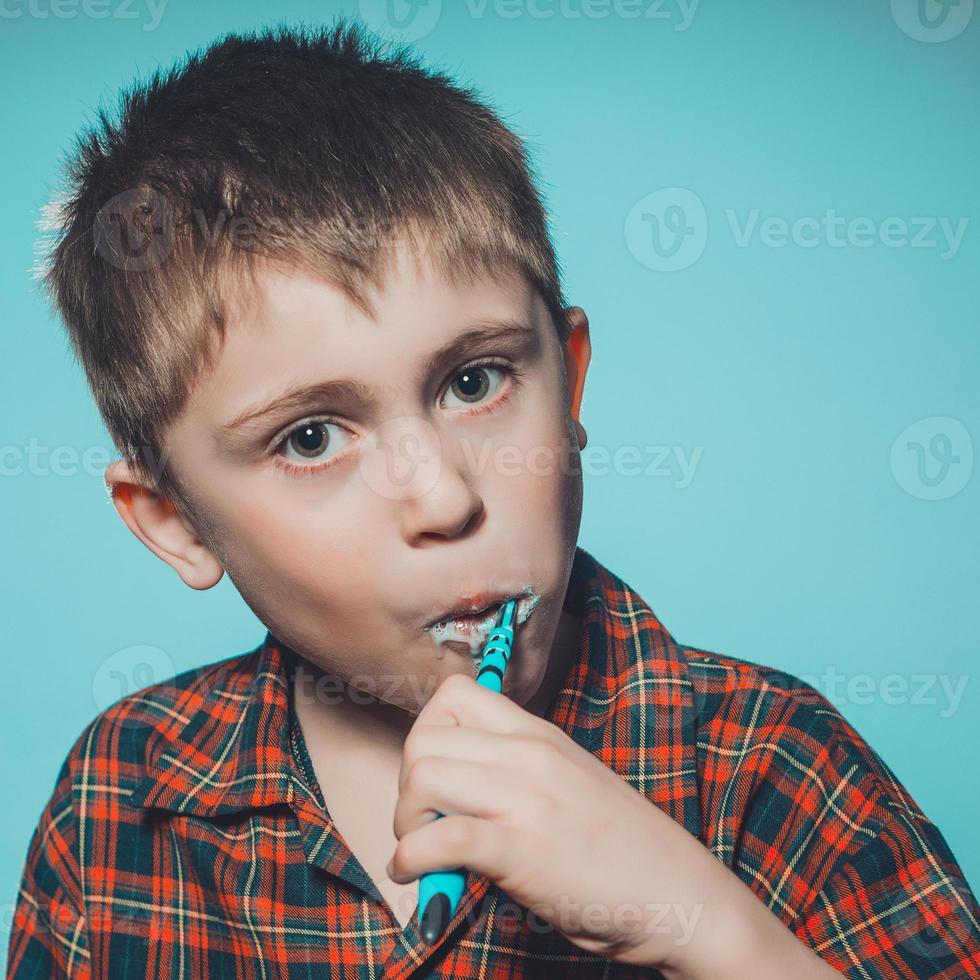 un' carino ragazzo nel un' pigiama spazzole denti con dentifricio prima di andare a dormire su un' blu sfondo foto