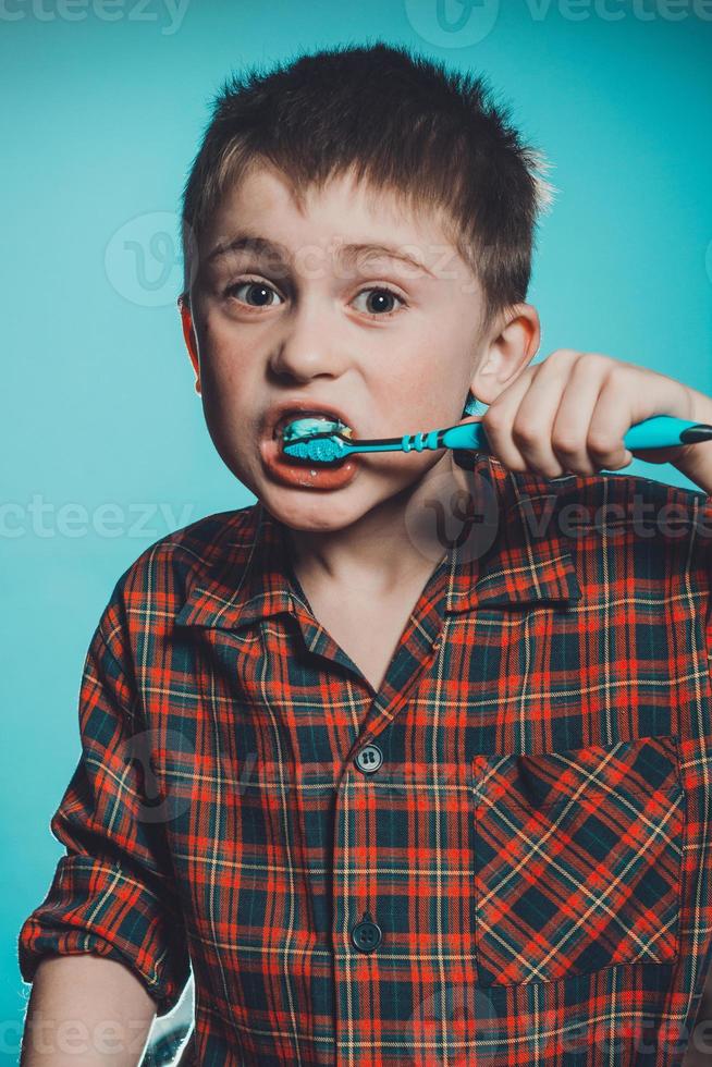 un' carino ragazzo nel un' pigiama spazzole denti con dentifricio prima di andare a dormire su un' blu sfondo foto