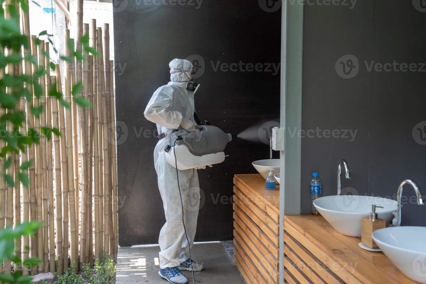 professionale tecnico uomo nel prevenzione completo da uomo con il suo sterilizzazione macchina e disinfezione acqua spray nel gabinetto o bagno la zona campo per purificazione coronavirus foto