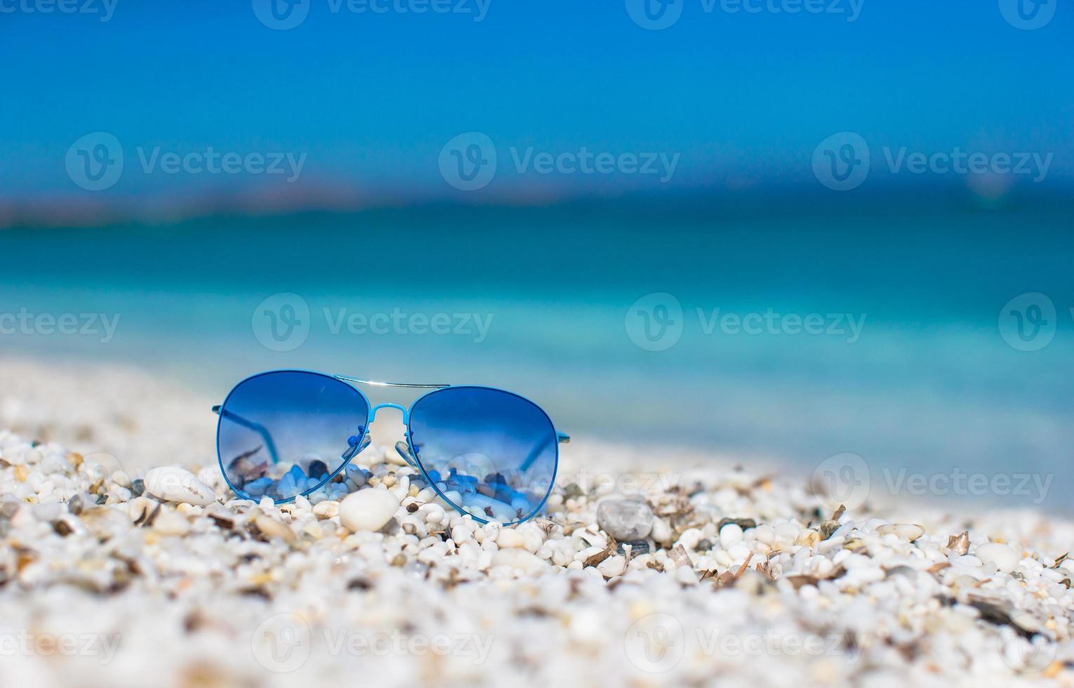 vicino su di colorato blu occhiali da sole su tropicale spiaggia. foto