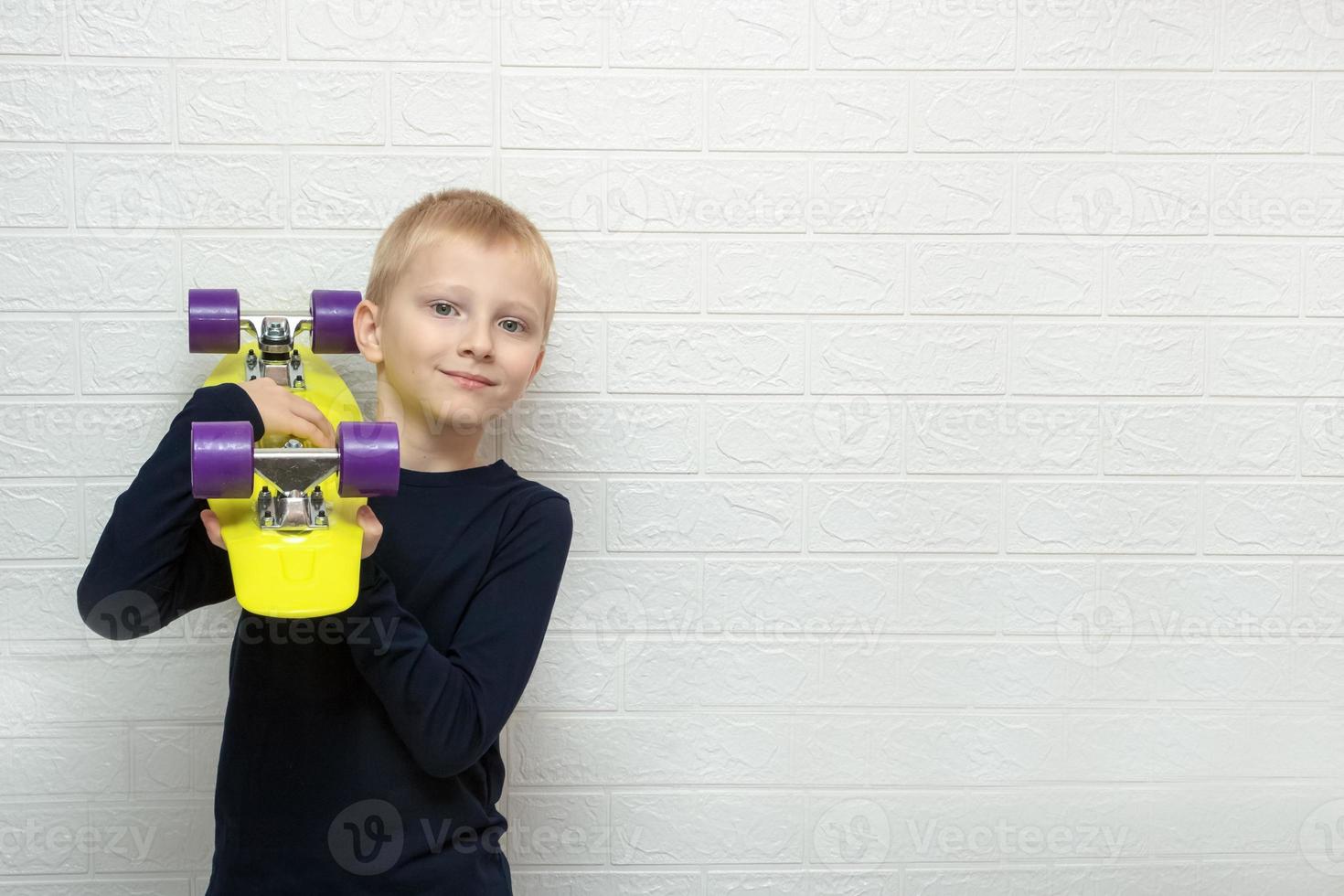 ragazzo detiene un' skateboard su il suo spalla contro il sfondo di un' parete con copia spazio, passione, gratuito tempo foto