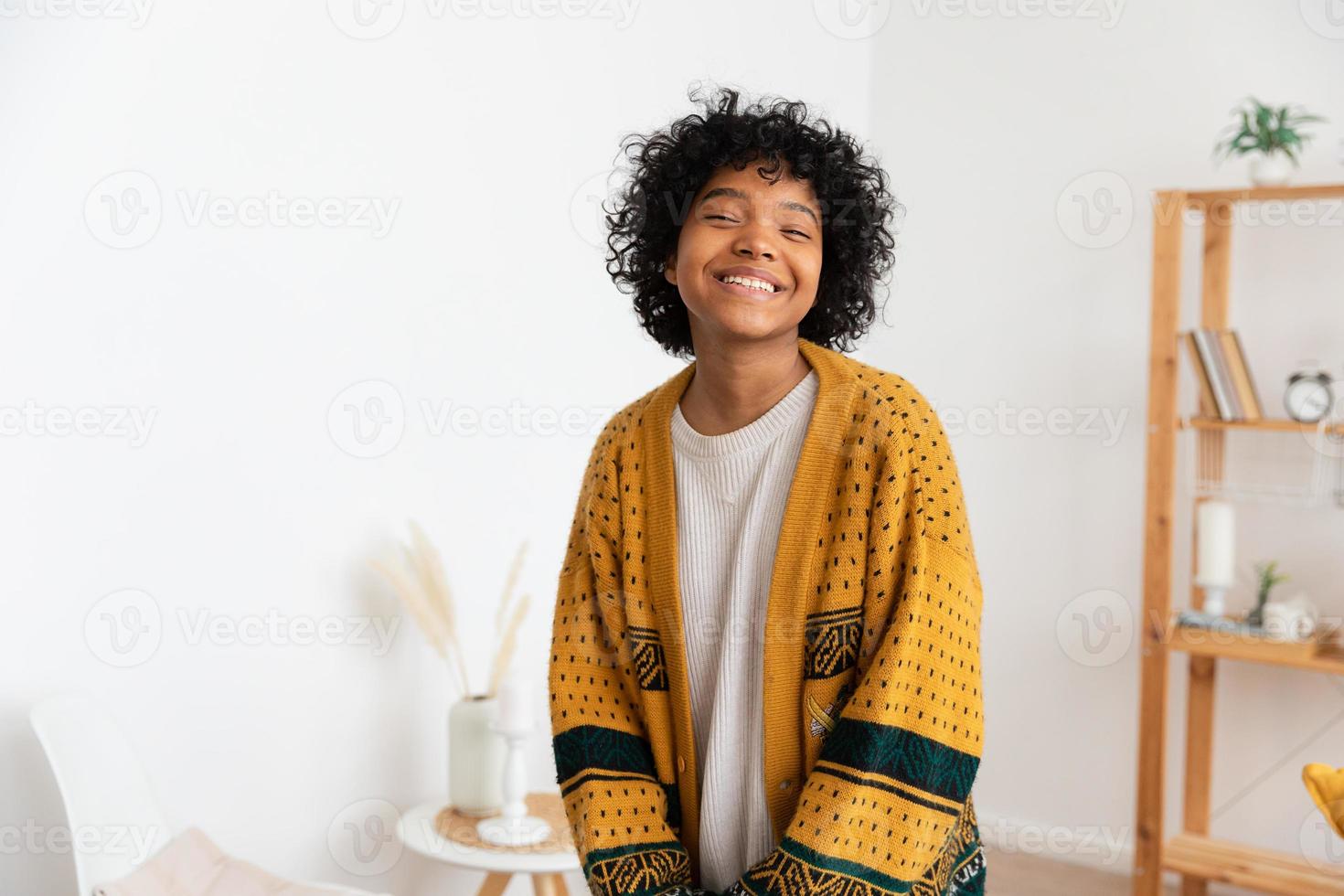 bellissimo africano americano ragazza con afro acconciatura sorridente a casa interno. giovane africano donna con Riccio capelli ridendo nel vivente camera. la libertà felicità spensierato contento persone concetto. foto