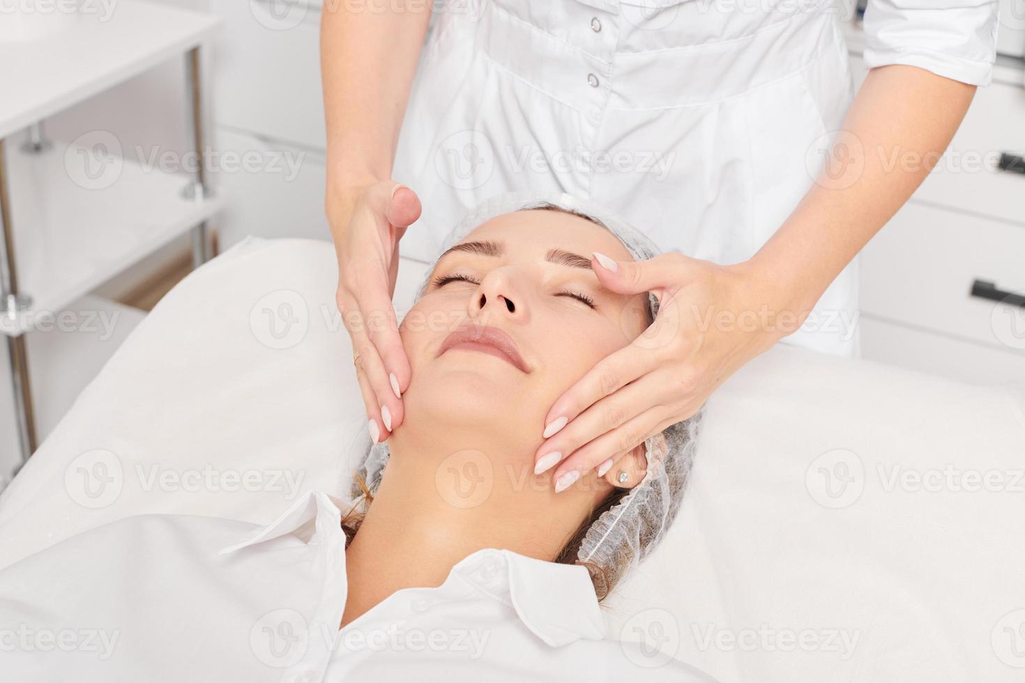 cosmetologo massaggi donna viso pelle dopo sfregamento idratante crema per ringiovanimento nel clinica foto