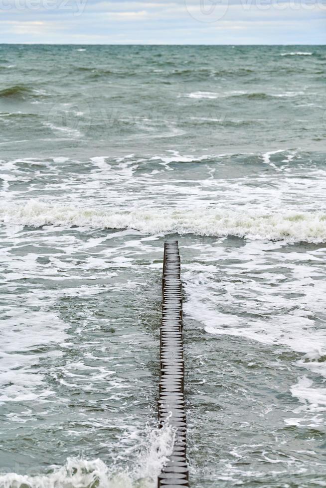 vista del mare blu con onde spumeggianti e frangiflutti in legno foto