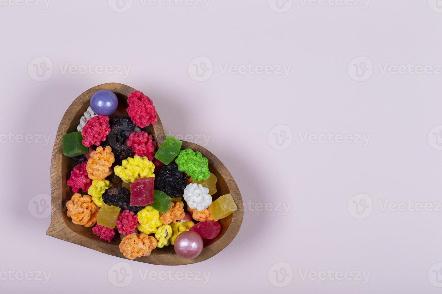 colorato dolci e caramelle siamo versato in un' a forma di cuore di legno vaso. foto