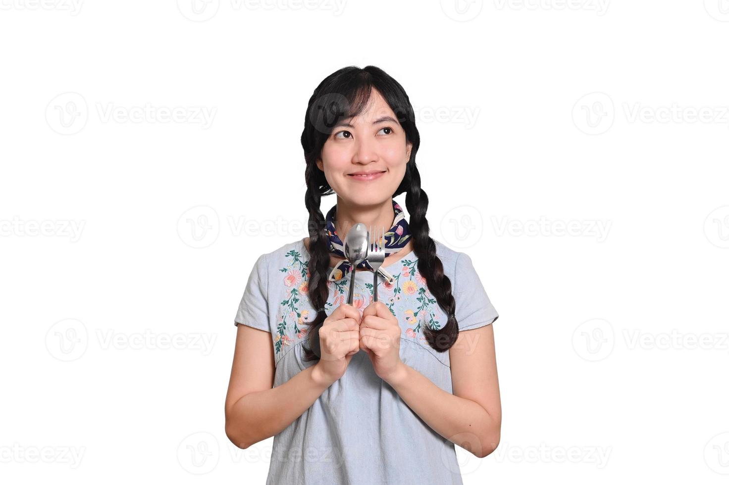 ritratto di bellissimo giovane asiatico donna Sorridi nel denim vestito con cucchiaio e forchetta su bianca sfondo foto