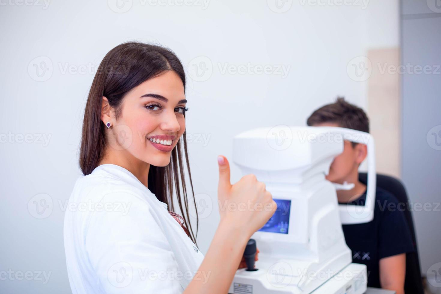 femmina oculista utilizzando macchina per controllo occhio vista nel clinica. poco ragazzo guardare a attrezzatura e medico analisi occhio allievo nel ottico negozio. concetto di occhio cura e Salute. foto