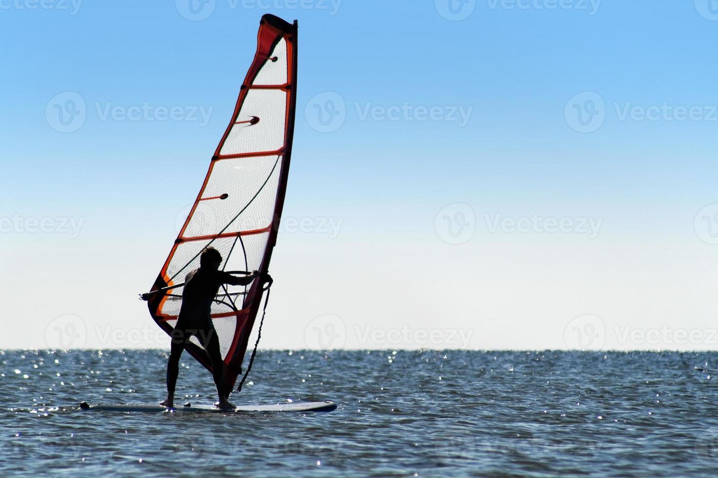 silhouette di un' windsurfista su il blu mare foto