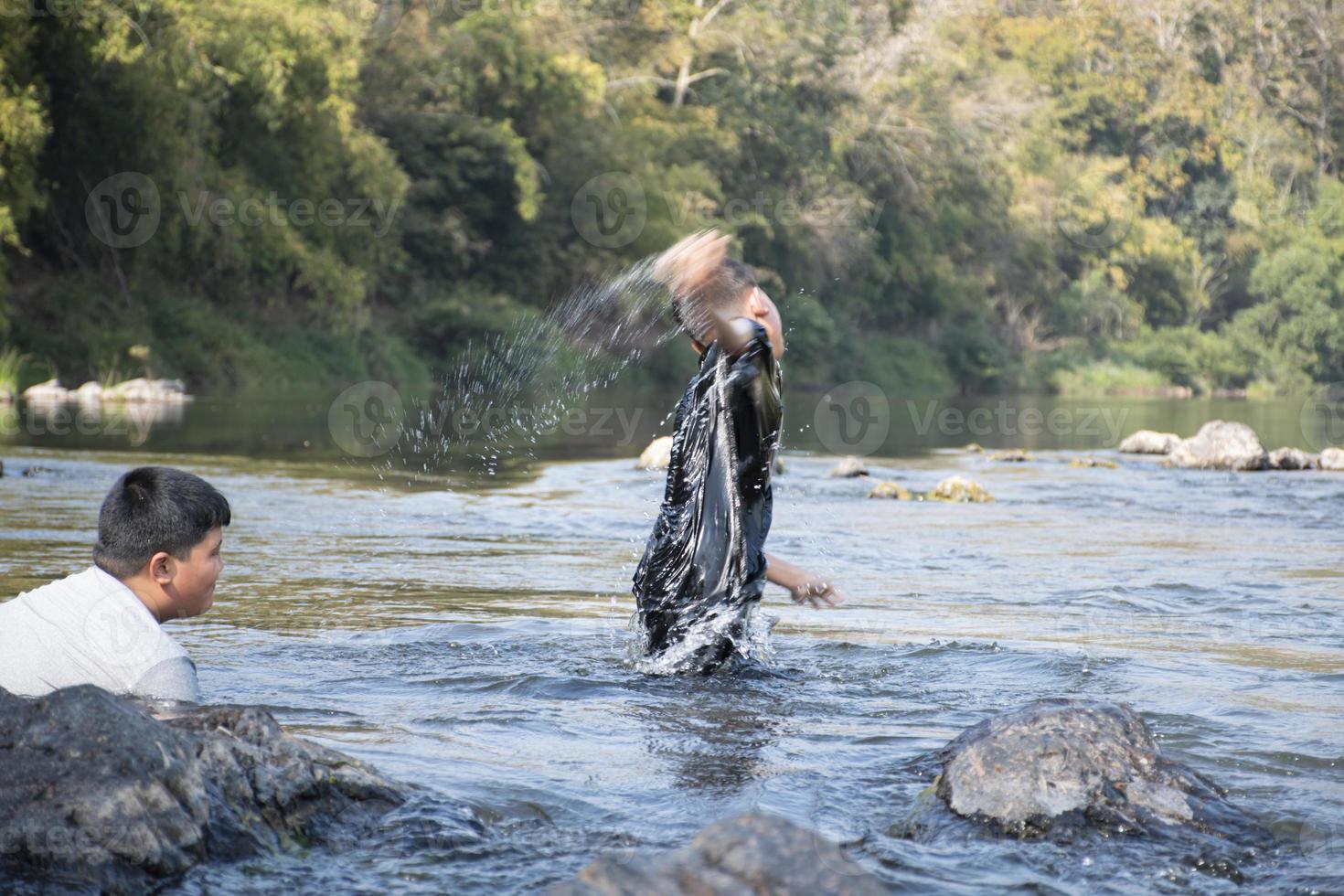 asiatico ragazzi siamo la spesa loro tempi liberi di immersione, nuoto, lancio rocce e attraente pesce nel il fiume insieme felicemente. passatempo e felicità di bambini concetto. foto