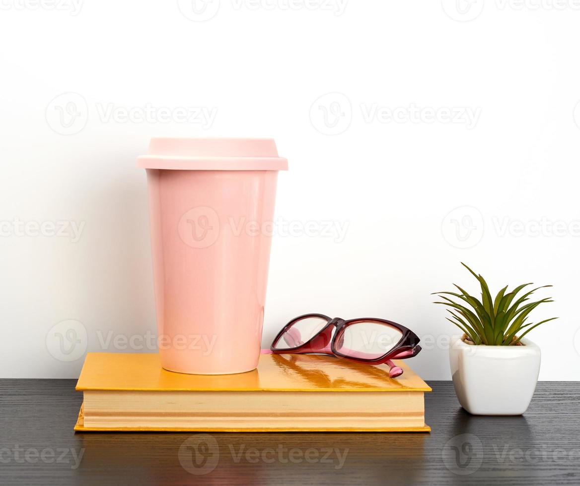 chiuso libro e rosa ceramica bicchiere con caffè su un' nero tavolo foto