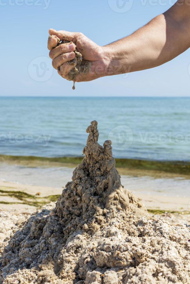 mano costruisce un' castello a partire dal il bagnato mare sabbia foto