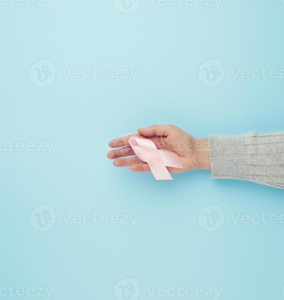 femmina mano detiene un' rosa a forma di arco nastro su un' blu sfondo foto