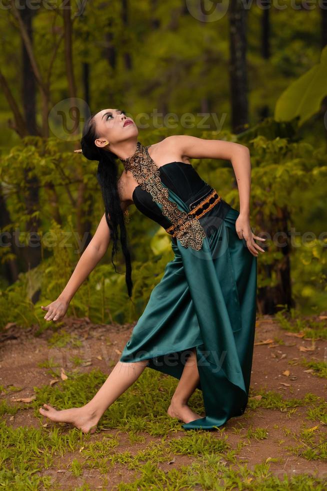 bellissimo asiatico donna nel un' verde costume con lungo nero capelli balli nel il boschi foto