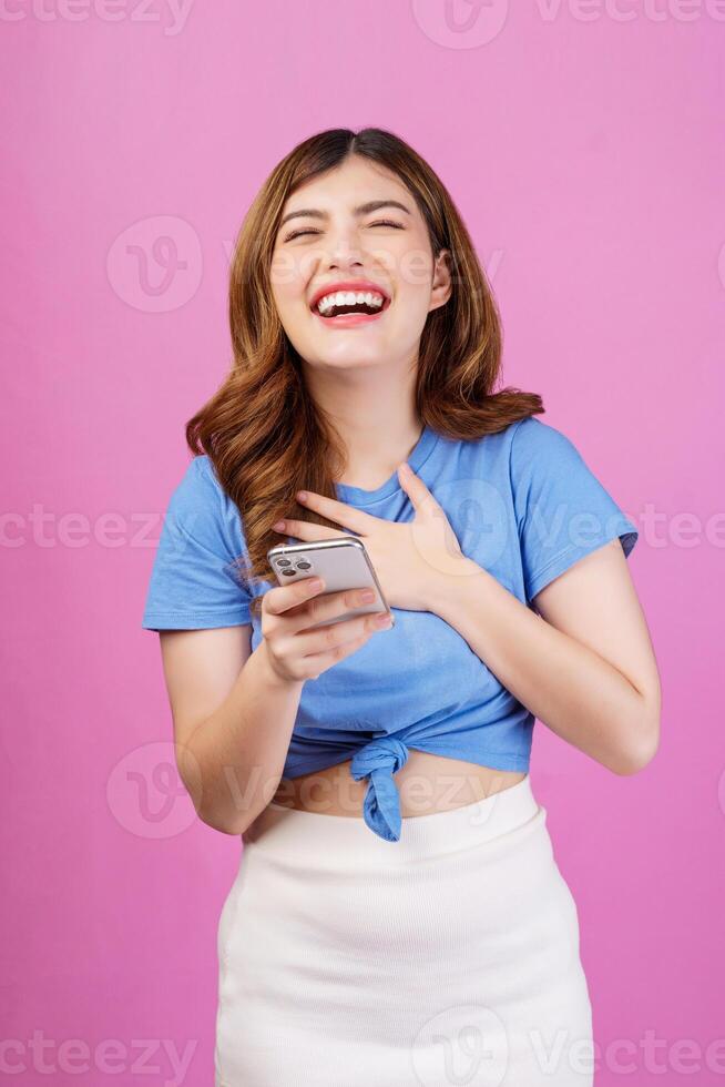 ritratto di contento giovane donna utilizzando mobile Telefono nel sua mani mentre in piedi isolato al di sopra di rosa sfondo foto