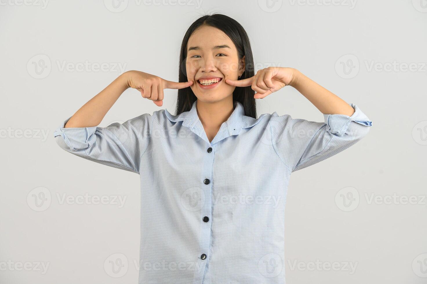 ritratto di contento giovane asiatico donna nel blu camicia sorridente dito guancia isolato su bianca sfondo foto