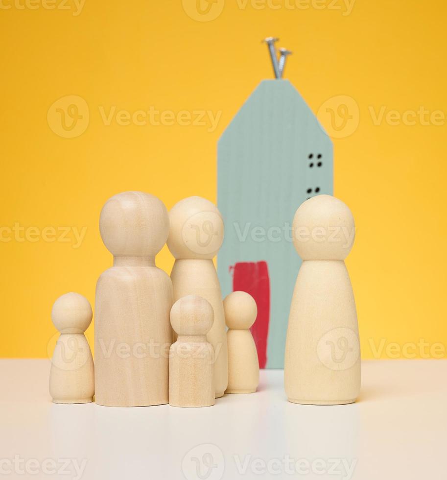 di legno Casa e miniatura figurine di un' famiglia e un' agente immobiliare su un' giallo sfondo. foto
