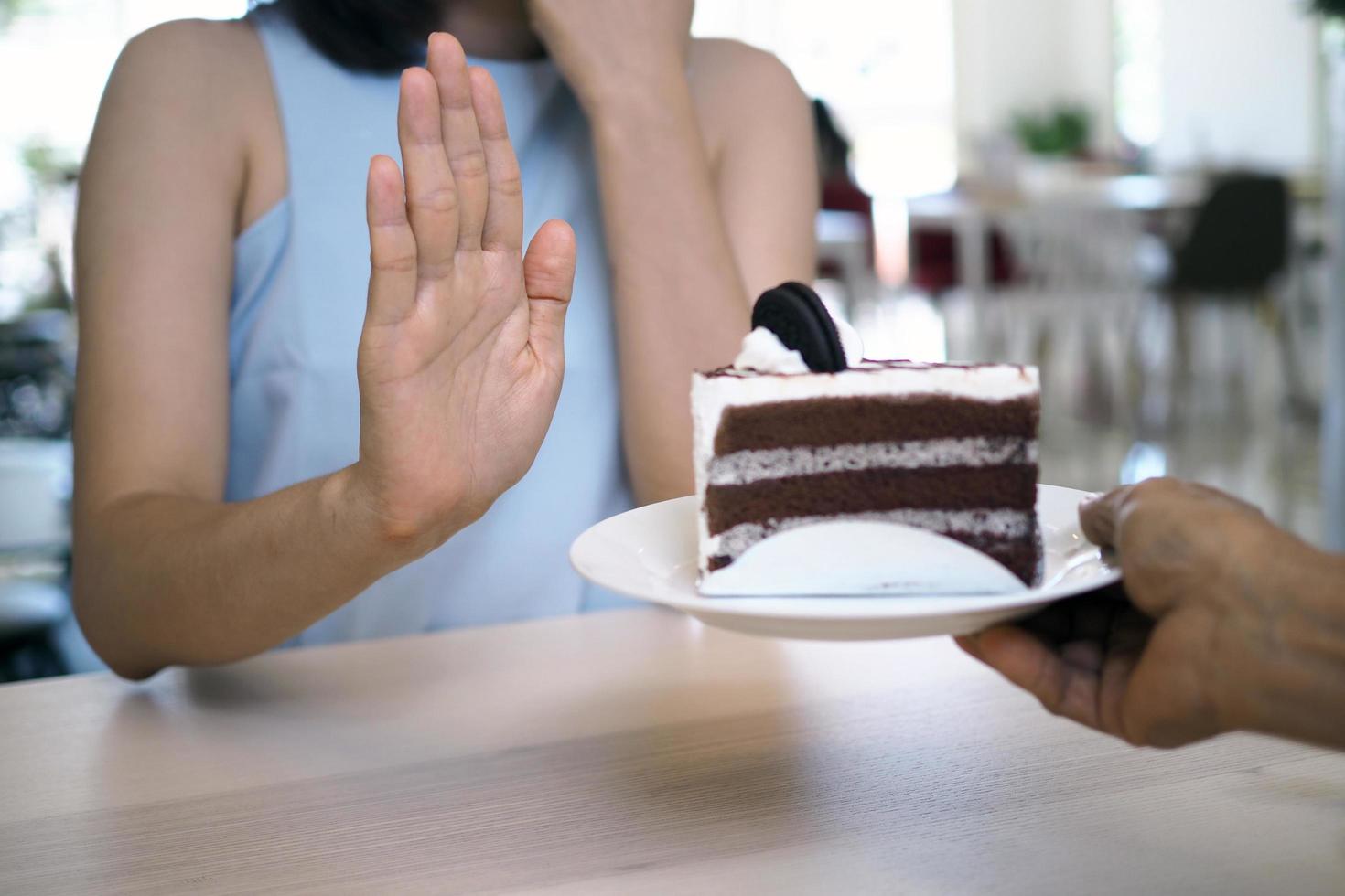 uno di il assistenza sanitaria ragazze Usato un' mano per spingere un' piatto di cioccolato torta. rifiuto per mangiare Alimenti quello contenere trans Grasso. foto