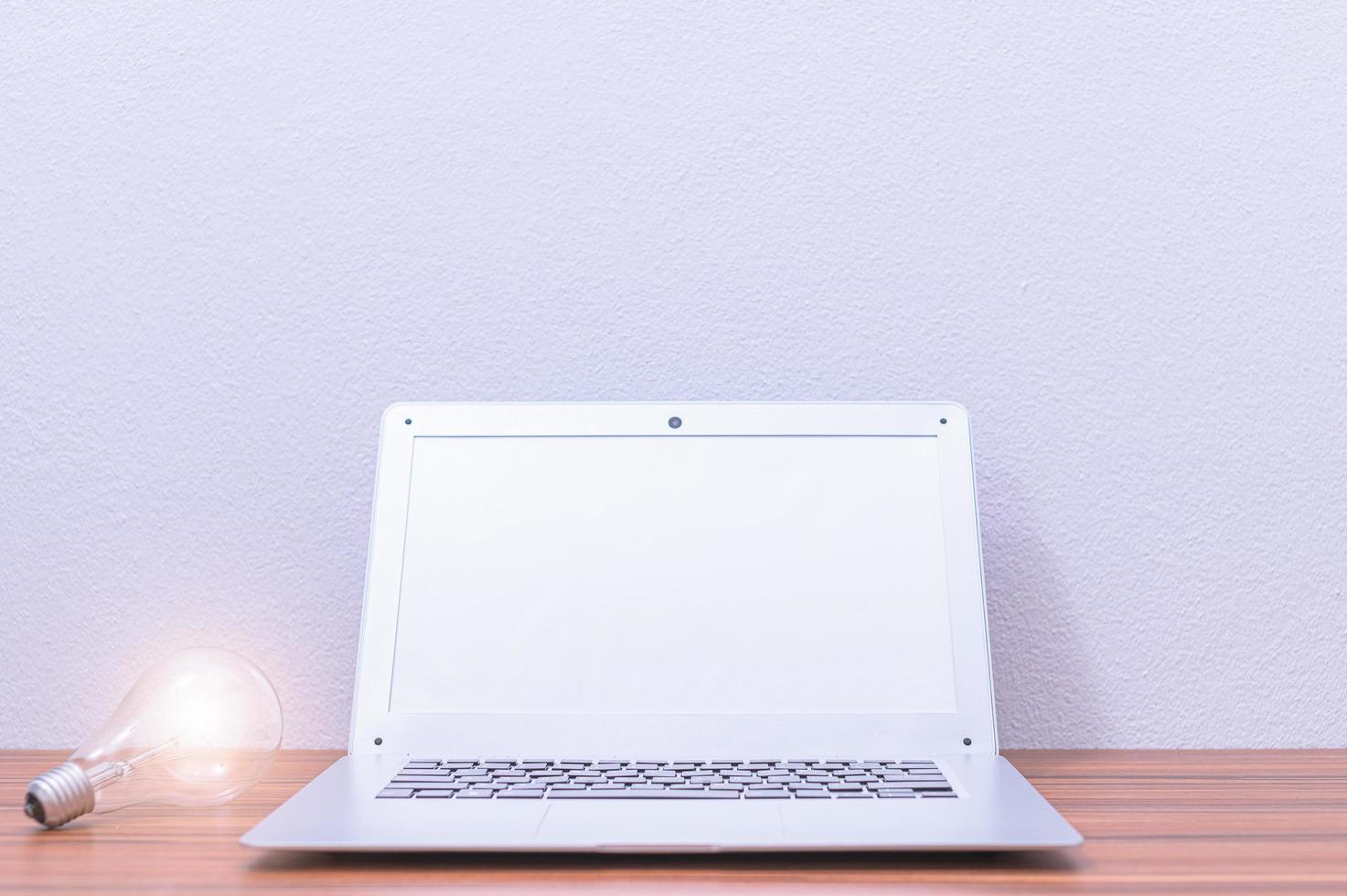 laptop e lampadina sulla scrivania foto