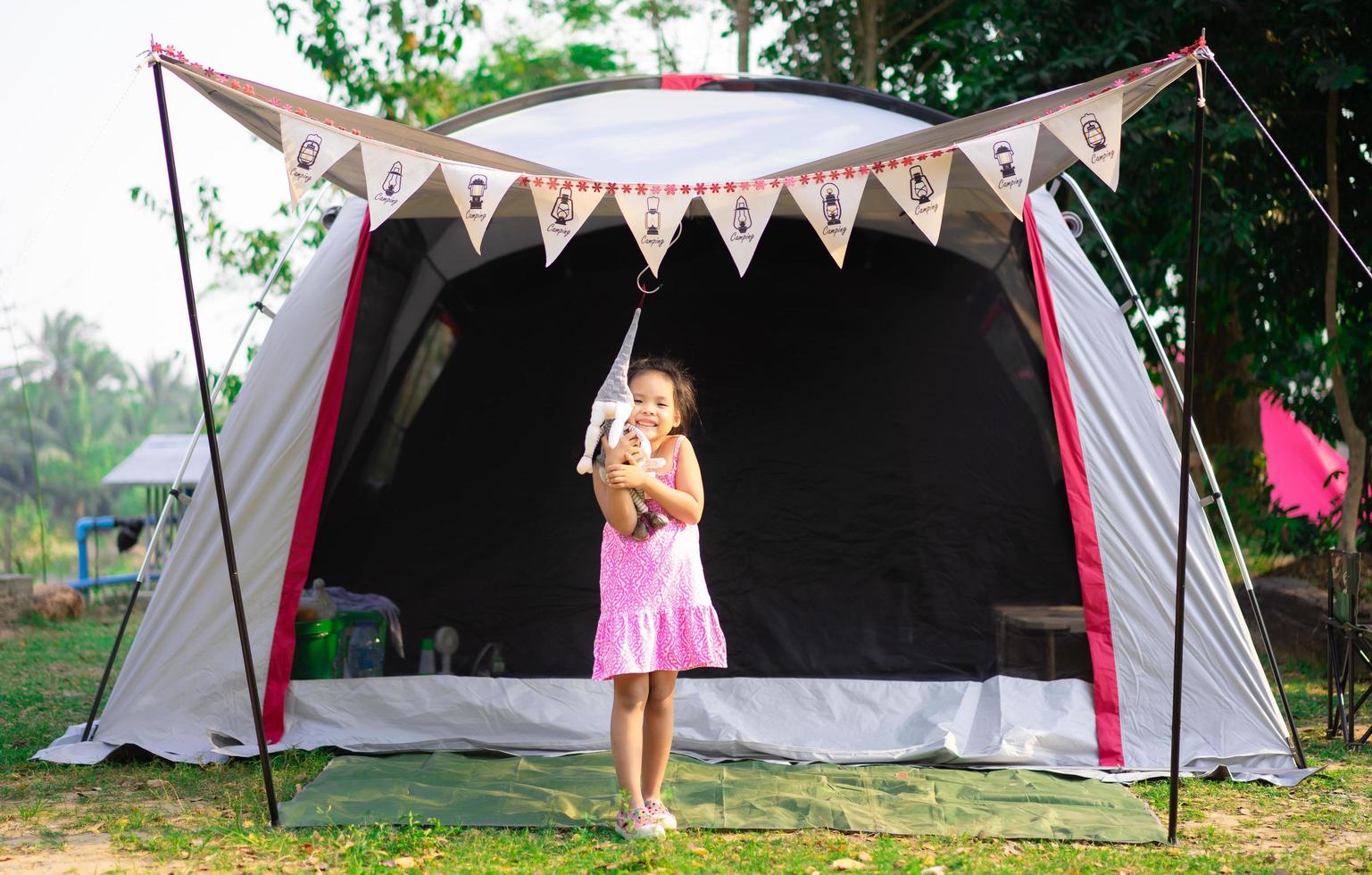piccola ragazza asiatica in piedi davanti alla tenda mentre va in campeggio foto
