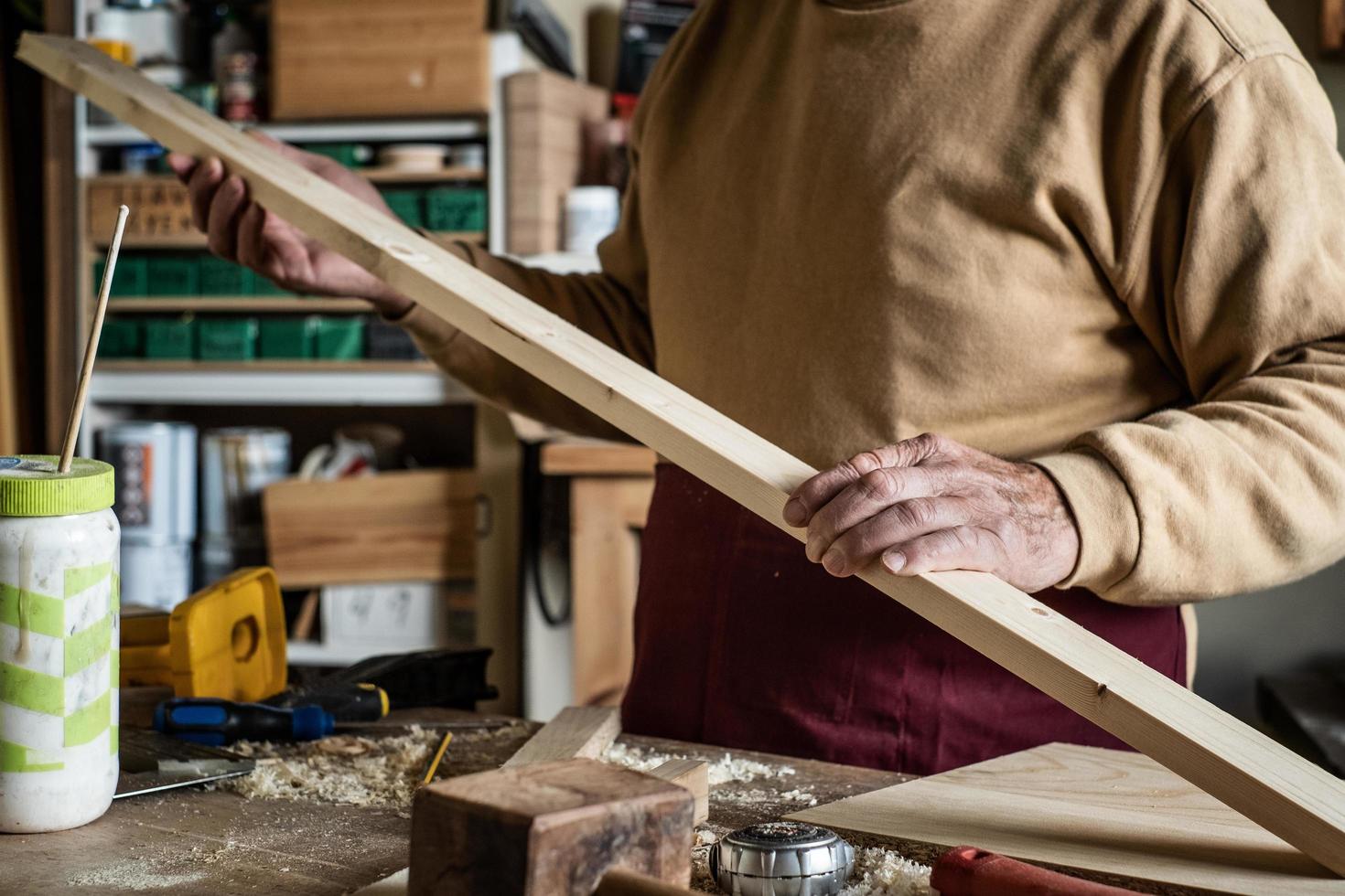 carpentiere guardando una tavola di legno in una falegnameria foto