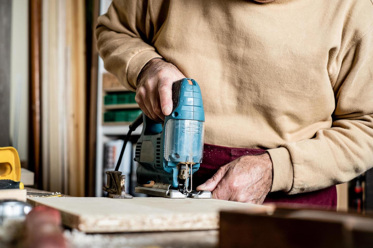 mani del falegname con il primo piano del puzzle elettrico. lavorare in un laboratorio di falegnameria. un uomo taglia il compensato con un seghetto alternativo elettrico. utensile elettrico per la lavorazione del legno. foto