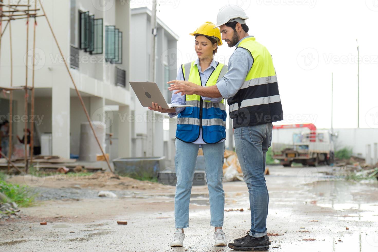 ingegnere uomo e femmina architetto indossare sicurezza caschi discutere alloggiamento sviluppo progetto a costruzione luogo utilizzando il computer portatile computer. contraente manager l'esame edificio tenuta infrastruttura. foto