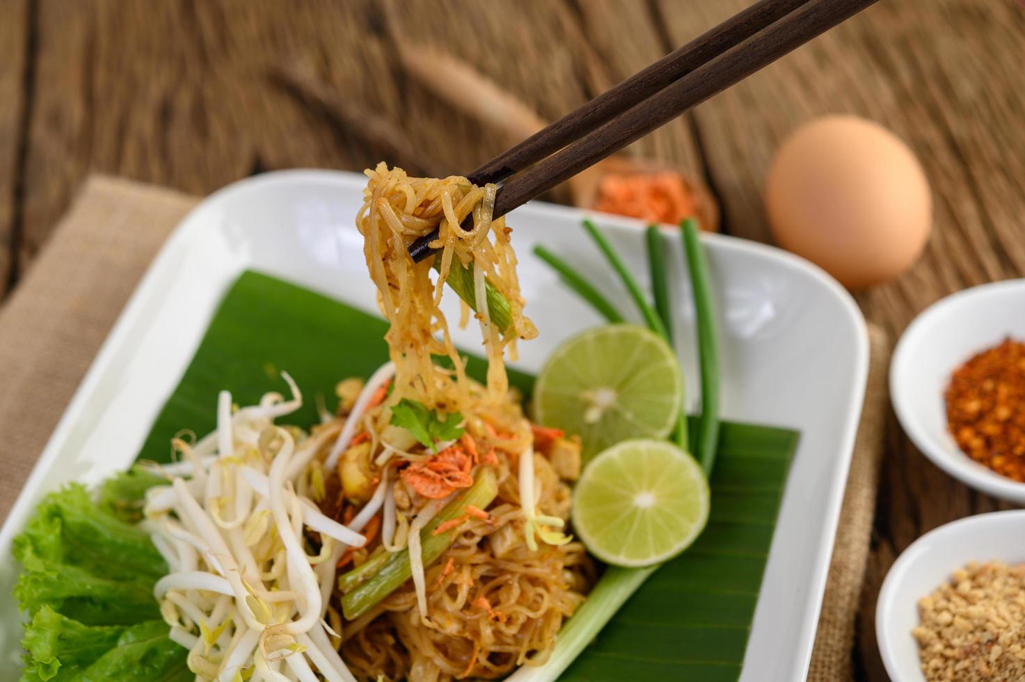 pad thai con limone, uova e condimento su un tavolo di legno foto