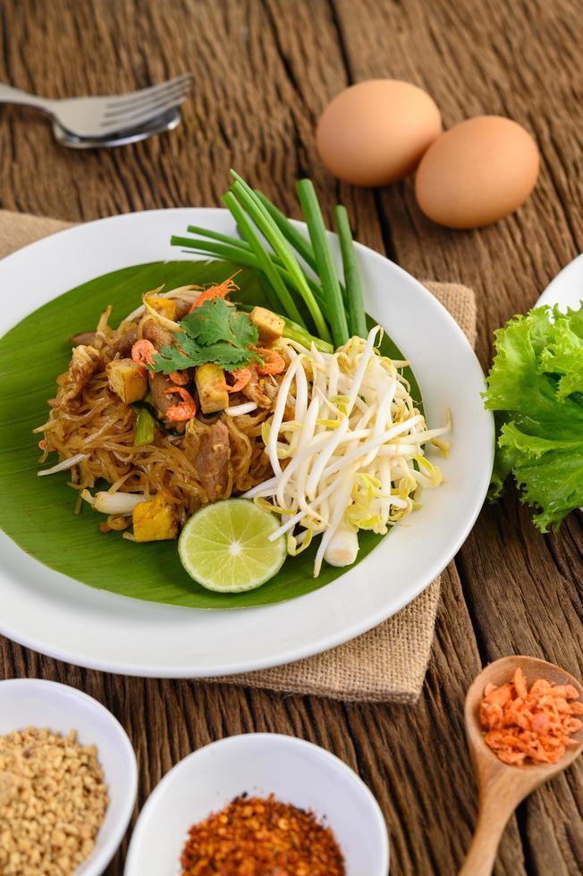 pad thai con limone, uova e condimento su un tavolo di legno foto