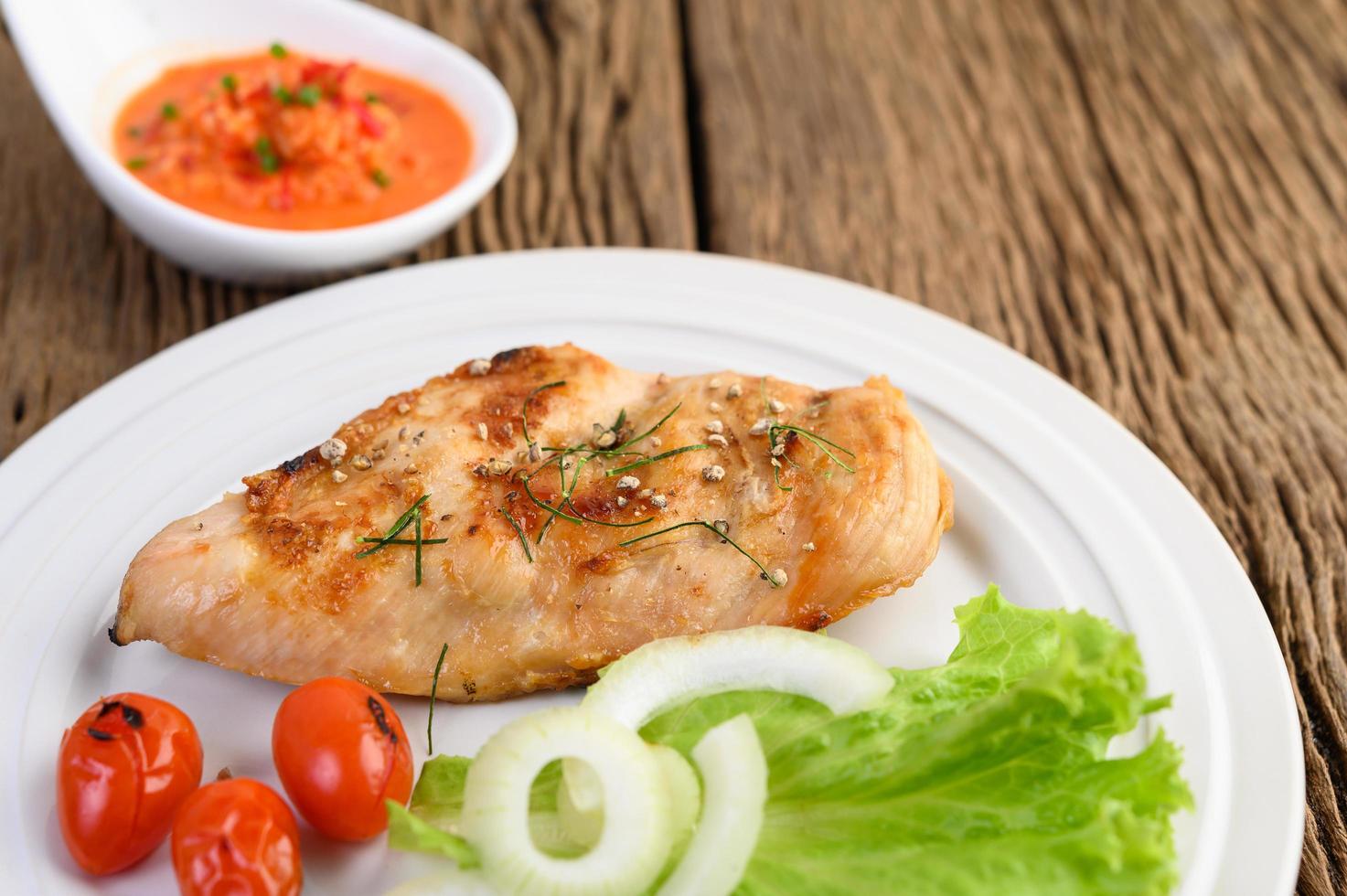 pollo alla griglia su un tavolo di legno con pomodori, insalata, cipolla e salsa di peperoncino foto