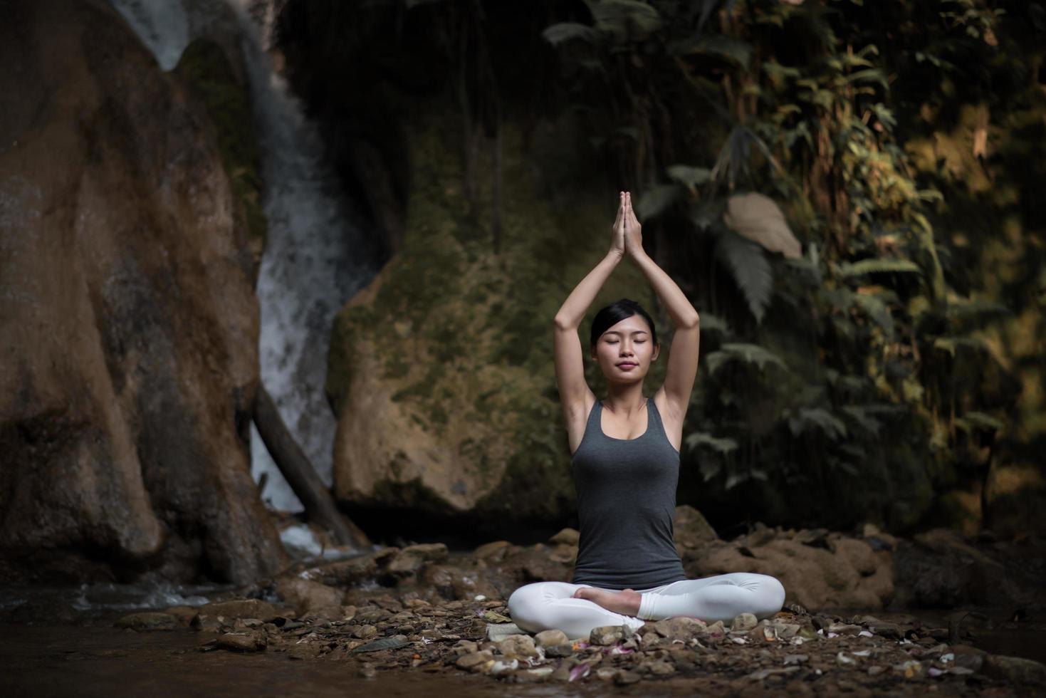 giovane donna in una posa yoga seduto vicino a una cascata foto