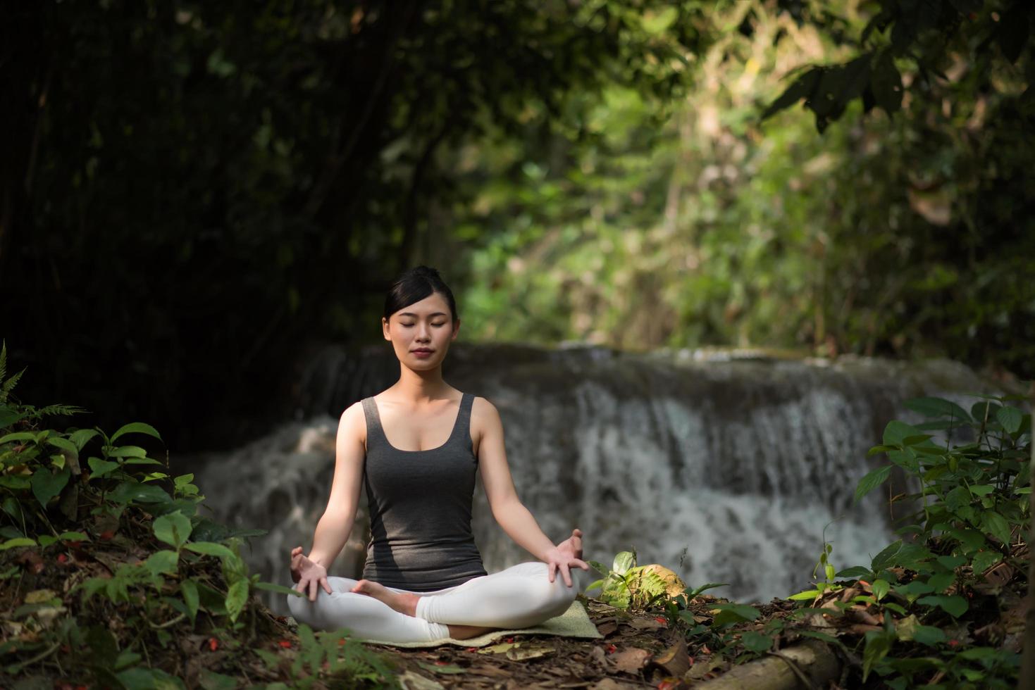 giovane donna in una posa yoga seduto vicino a una cascata foto