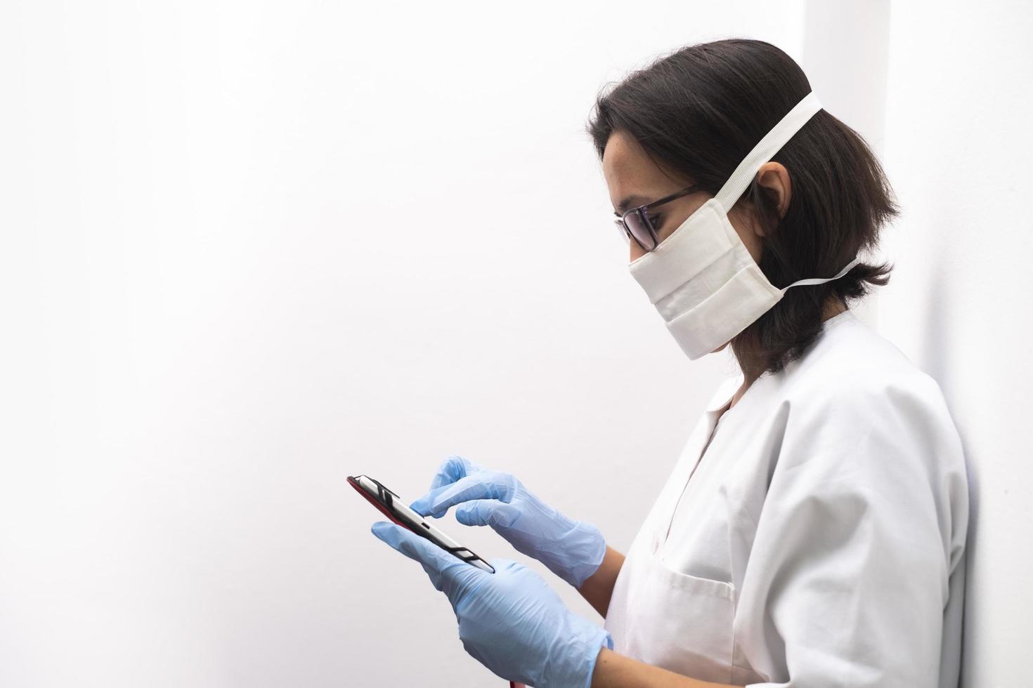 infermiera che indossa una maschera e guanti blu utilizzando un tablet in ospedale foto