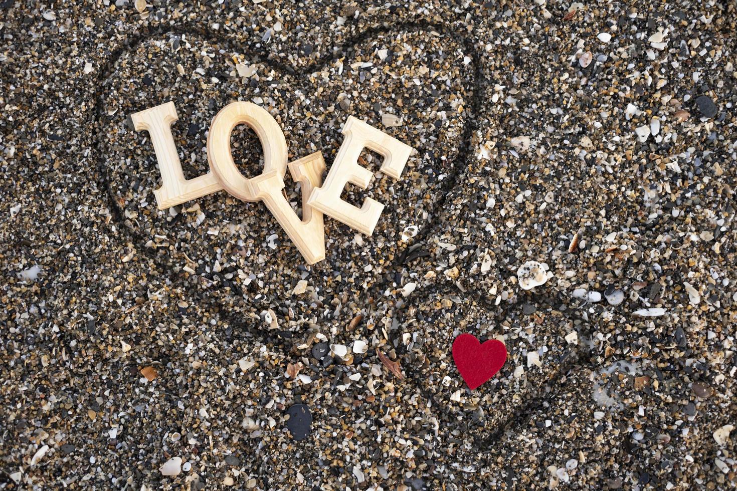 lettere di legno che compongono la parola amore con un cuore rosso su uno sfondo di spiaggia di sabbia, all'interno di un cuore fatto con le dita. concetto di san valentino foto