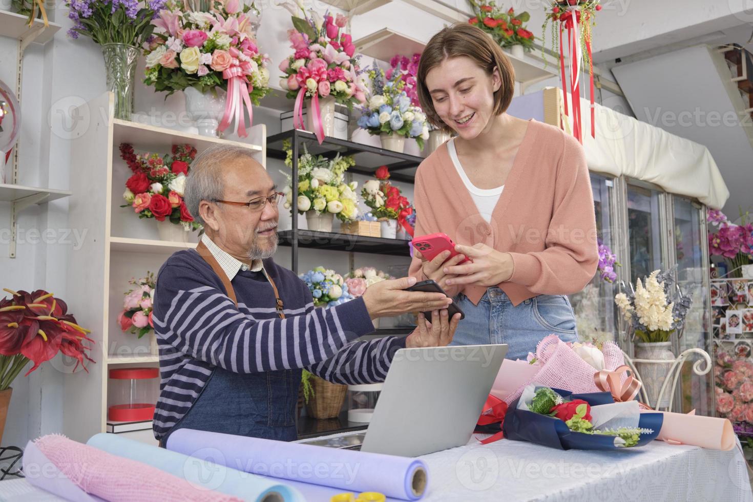 senza soldi attività commerciale imprenditore. bianca cliente donna shopping e digitale pagamento di lettura un' mobile Telefono applicazione per un asiatico anziano maschio fioraio proprietario. bellissimo floreale negozio, inteligente pmi negozio. foto