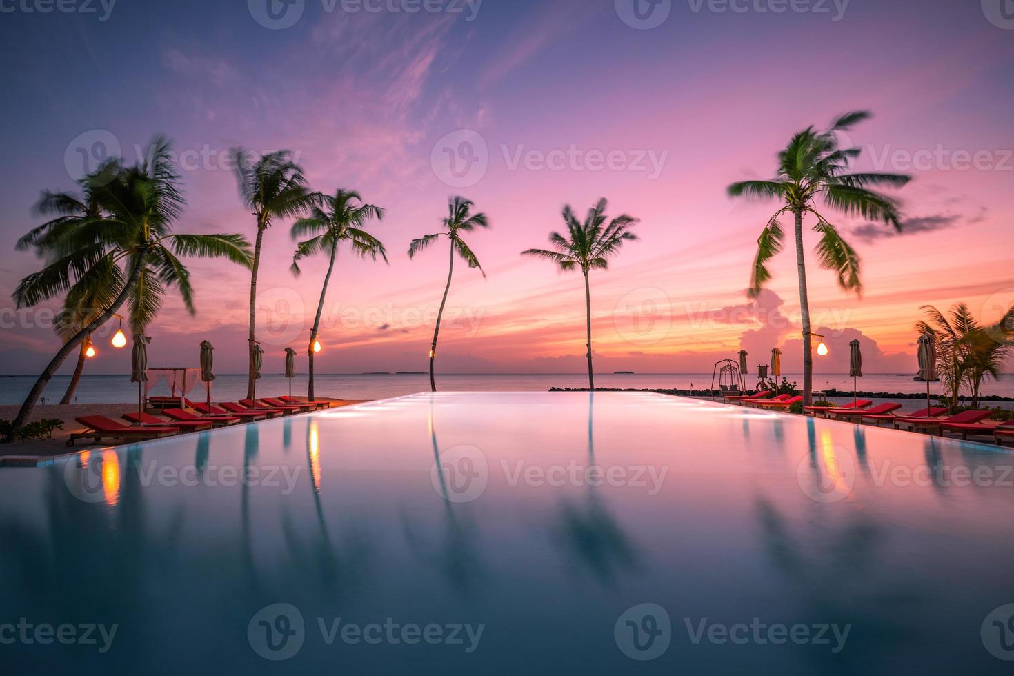 bellissimo bordo piscina e tramonto cielo. lussuoso tropicale spiaggia paesaggio, ponte sedie e lettini e acqua riflessione. palma alberi riflessione, sorprendente lusso estate spiaggia paesaggio. spiaggia tramonto foto